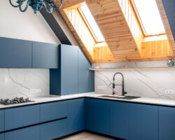 Full vertical view with skylights, timber ceiling and a minimalist handleless suite in blue. A classic chandelier adds an eclectic touch to the contemporary space.